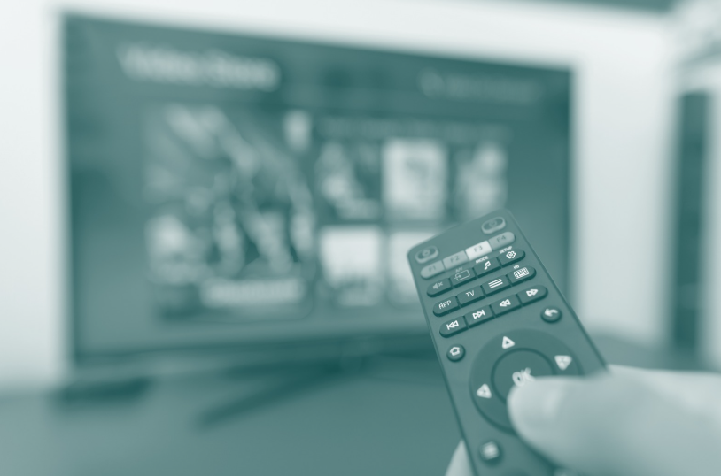 Hand holding remote control against background of TV set in living room